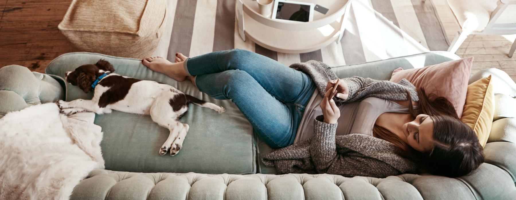 woman texting while lying on a couch with her dog